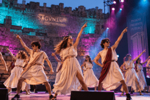Estudiantes con túnicas griegas bailando en un escenario con luces modernas frente al Teatro Romano de Sagunto